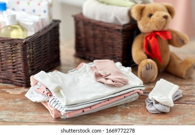 Babyhood And Clothing Concept - Baby Clothes, Teddy Bear Toy And Baskets On Wooden Table At Home