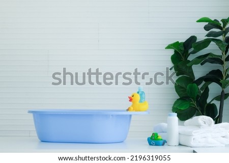 Baby's bath is placed on the table with duck toys and towels and can of powder.