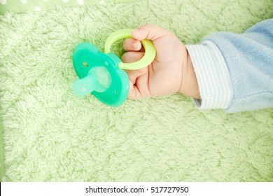 Baby's cute little hand and plastic baby soother pacifier on green blanket. Concept of childcare, joy, hope, love, pacify, bonding and care...