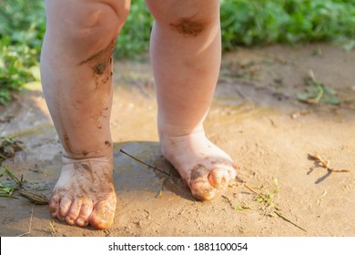 Baby's Dirty Feet On The Path. On A Hot Summer Day, A Child Runs Barefoot. Dirt, Earth, Water Drops On The Baby's Feet And Knees. Walking On The Grass Without Shoes.