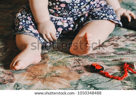 Baby's feet. Baby girl sitting on the couch. Girl in beautiful floral dress. Tiny hands and feet. Cozy morning. Childhood and parenthood. One year old baby.