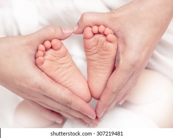 Baby's Foot In Mother Hands Closeup On The Bed, New Family And Baby Healthy Concept