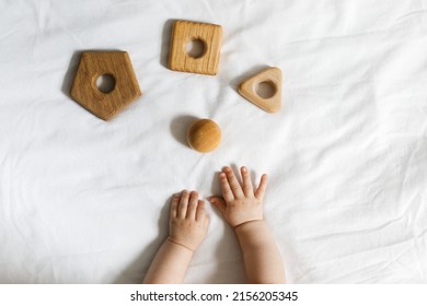 Baby's hands and wooden toys on a white fabric background, early child development