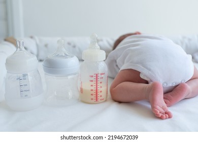 Baby's Little Butt With Bend Up Legs And Bottle With Milk Formula On White Blanket. Newborn - Happiness For Family. Concept Of Food For Baby. Choice Bottles. Problems Of Gases And Farts.