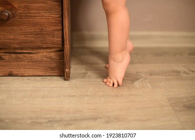 The Baby's Small Feet Are On The Floor Standing In Tip Toe In Front Of The Dresser. High Quality Photo