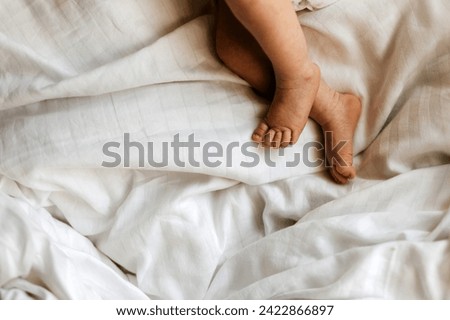 A baby's tiny feet and toes on soft white cotton bedsheet.