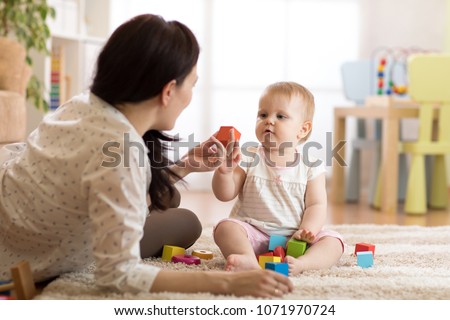 Babysitter and baby girl playing with toy cubes at home