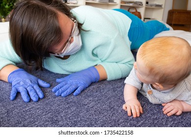 Babysitter In Mask And Gloves Entertaining Baby At Home Interior, Playing With Child On Floor, Training To Crawl. Quarantine Or Babysitting Concept