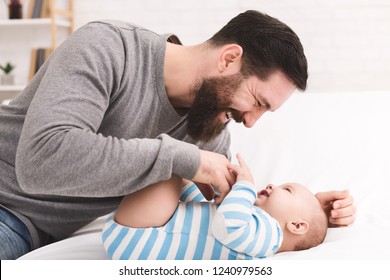 Babysitting is fun. Father tickling and snuggling his newborn son on bed at home