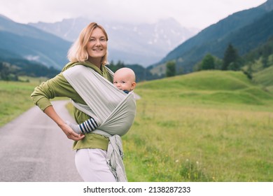 Babywearing. Mother and baby on nature outdoors. Baby in wrap carrier. Woman carrying little child in baby sling in green mint color. Concept of green parenting, natural motherhood, postpartum period. - Shutterstock ID 2138287233