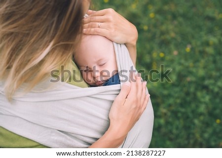 Babywearing. Mother and baby on nature outdoors. Baby in wrap carrier. Woman carrying little child in baby sling in green mint color. Concept of green parenting, natural motherhood, postpartum period.