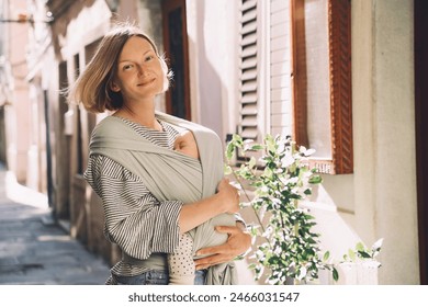 Babywearing. Mother and baby walking in town. Baby in wrap carrier. Young woman carrying little child in baby sling in mint color. Concept of green parenting, natural motherhood, postpartum period. - Powered by Shutterstock