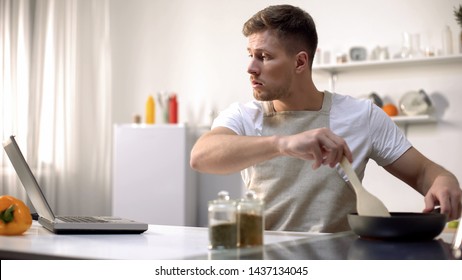 Bachelor Preparing Meal In Pan, Reading Recipe And Cooking Tips Online, Courses