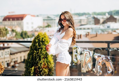 Bachelorette Party. Happy Future Bride In A White Shirt And Shorts Poses On The Roof Of The House Overlooking The City.