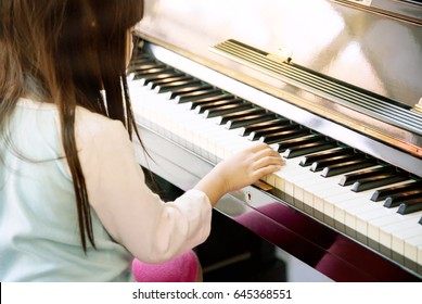 Back Of Adorable Female Kid Playing Piano At Home. Close Up Of Asian Cute Girl Practicing Piano In Music Class. 