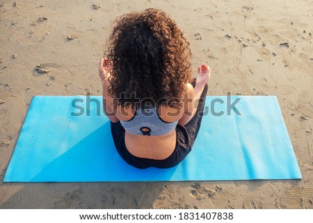 back of afro america woman with curly hair deep breathing and calming herself on empty morning beach after surya namaskar