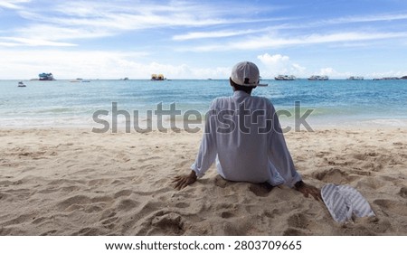 back alone man sitting on beach and blue sea and sky background, relaxing on vacation at Koh larn, Pattaya, Thailand