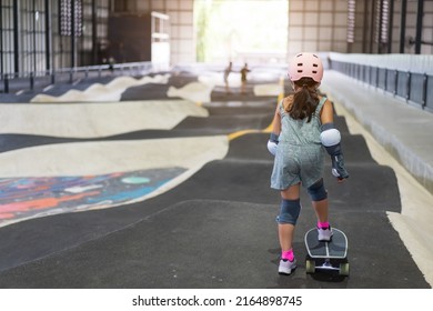 back asian child or kid girl playing surf skate or skateboard and start on indoor pump track in skatepark by extreme sports to wearing helmet elbow pads wrist and knee support for body safety protect