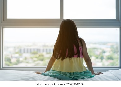 Back Asian Children Or Kid Girl Sitting Alone On White Bed And Lonely Depressed Or Suppressed Young Woman And Sad Child In Bedroom At Home With Morning Warm Sunlight On Window And Wake Up Late In City