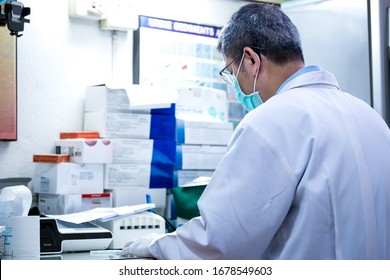 Back Of Asian Male Doctor  Writing Observations , Sitting At Messy Desk  . Work Hard For Researching About Covid-19.