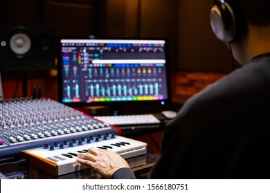 back of asian male music producer arranging a song on midi keyboard and computer in home recording studio. music production concept - Powered by Shutterstock