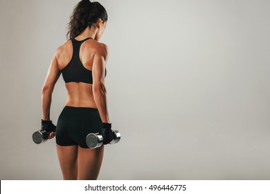 Back of athletic woman with muscular physique holding pair of chrome finished dumbbells over gray background with copy space - Shutterstock ID 496446775