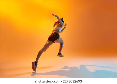 Back bottom view of young girl, professional runner, athlete training over orange studio background in neon light. Concept of sportive lifestyle, health, endurance, action and motion. Ad - Powered by Shutterstock