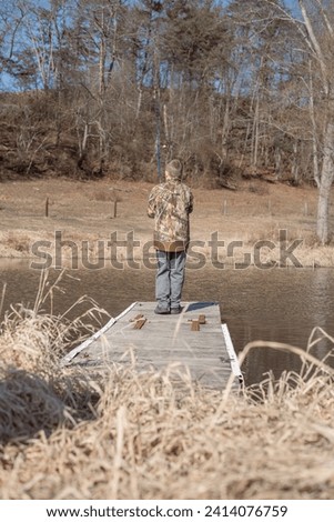 Back of boy casting fishing rod from dock in pond