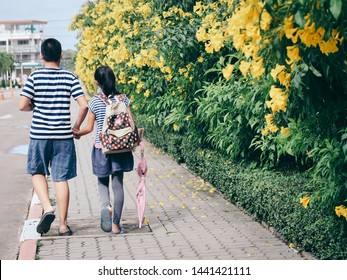 Back of brother holding his sister walking along the road with yellow flower background.