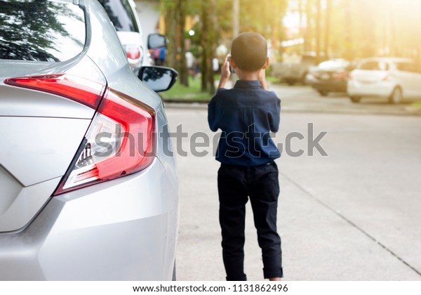 Back of car stop in parking\
lot inside garden park on concrete floor with boy stand beside\
car.