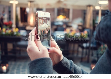 Back close up view of female person holding cellphone with and make photo with street on background. Woman's hands with mobile phone devise, finger touching display