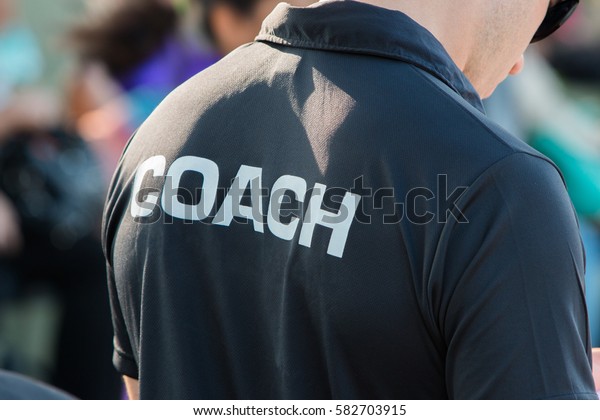 back of a coach\'s black shirt with the white word\
Coach written on it