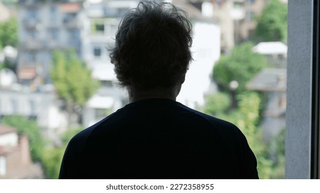 Back of a contemplative senior man looking out window. Pensive older person standing at home staring at view in silhouette - Powered by Shutterstock