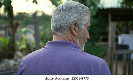 Back Of Contemplative Senior Man Walking Forward In Nature. Pensive Older Person Walks Outdoors In Contemplation