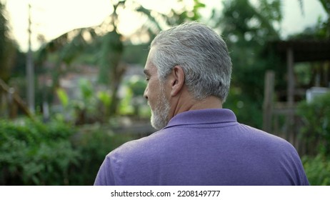 Back Of Contemplative Senior Man Walking Forward In Nature. Pensive Older Person Walks Outdoors In Contemplation