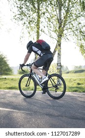 Back of a cyclist with a backpack while riding in the city on a bike. Man in sportswear and a helmet rides the city park.