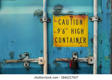 The Back Door Of Blue Heavy-duty Container With Locks And Sealed Padlock. Container Is Very Rusty And Aged. Yellow Warning Sign About High Container Height Is Marked On The Door