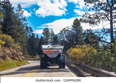 Back Of Dump Truck Emitting Smoke Behind And Dust On Top Driving On Curvy Mountain Road - Selective Focus