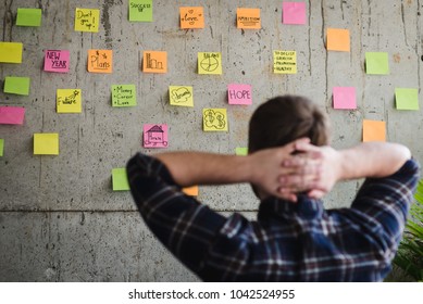 Back of entrepreneur sitting in office and look at colorful sticky message on cement wall. Work lifestyle concept.  Selective focus. - Shutterstock ID 1042524955