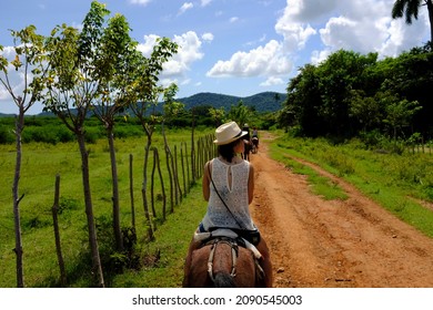 The back of a European female tourist riding on a horse through a dirt terrain outside of Trinidad, Cuba. - Shutterstock ID 2090545003