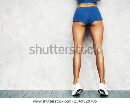 Back of fitness woman in sports clothing looking confident.Young female wearing sportswear. Beautiful model with perfect tanned body.Female posing in studio near gray wall