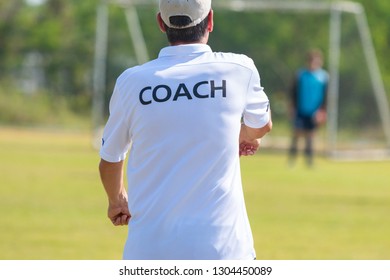 Back Of Football Coach Wearing White COACH Shirt At An Outdoor Sport Field Coaching His Goalie Player During A Game, Good For Sport Or Coaching Concept