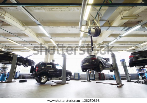 Back of four black cars in garage with special\
equipment for repair.