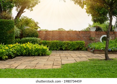 Back and front yard cottage garden, flowering plant and green grass lawn, brown pavement and orange brick wall, evergreen trees on background, in good care maintenance landscaping in park  - Shutterstock ID 1980734459
