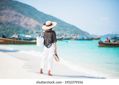 Back Of Full Body Woman Casual Look Wearing Hat And Holding Shoe On Sunny Beach With Sea And Boats In The Background. Concept Of Holidays And Travel. Picture Looking Alone Or Sad. She Looking Forward.