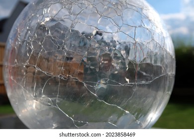 Back Garden And Blue Cloudy Sky Viewed Through A Spherical Or Round Cracked Or Fractured Glass Flower Vase. Reflected, Distorted And Refracted Light.