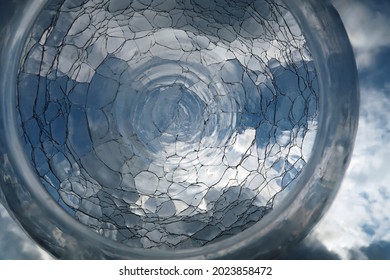 Back Garden And Blue Cloudy Sky Viewed Through A Spherical Or Round Cracked Or Fractured Glass Flower Vase. Reflected, Distorted And Refracted Light.