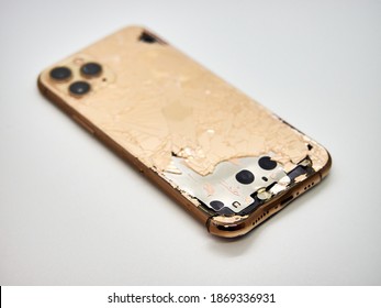 The back of gold smartphone iPhone 11 Pro with a broken glass and a damaged curved body close-up isolated on white background