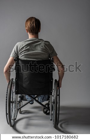 Back of guy with physical inability sitting in wheelchair. He is holding his hands on wheels