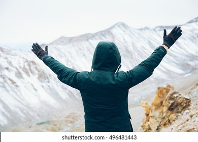 Back Of Happy And Cheerful Man In Coat Standing And Raising Hands Up In Snowy Mountain Scenery - Freedom Concept.